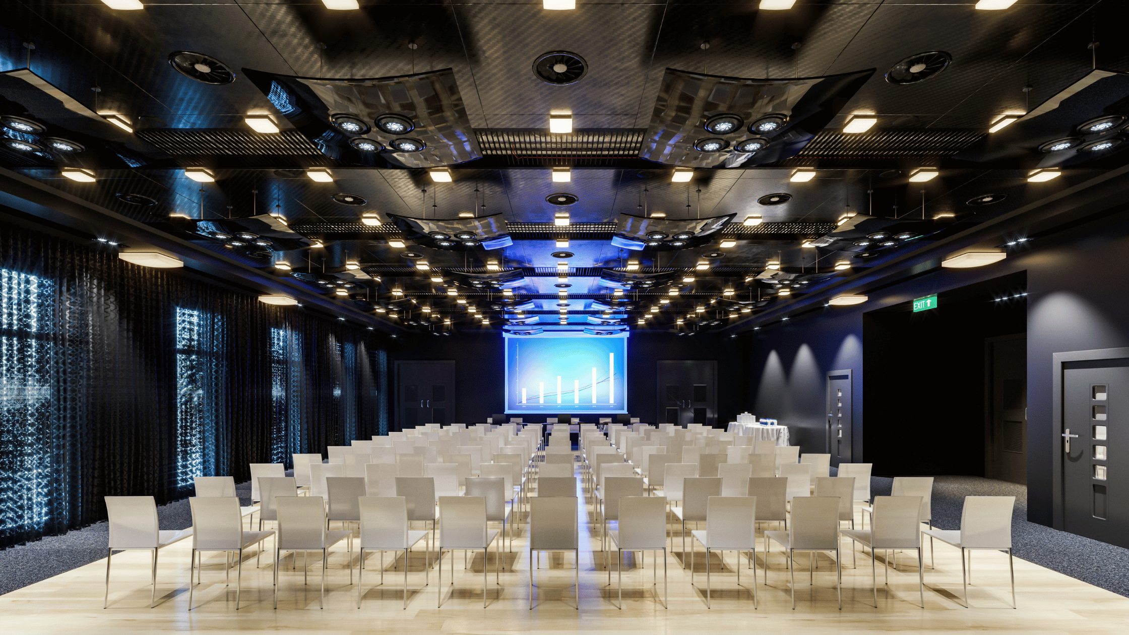A conference room with rows of white chairs facing a large screen displaying a bar graph. The room has dark walls, a reflective ceiling with multiple lights, and blue lighting accents.