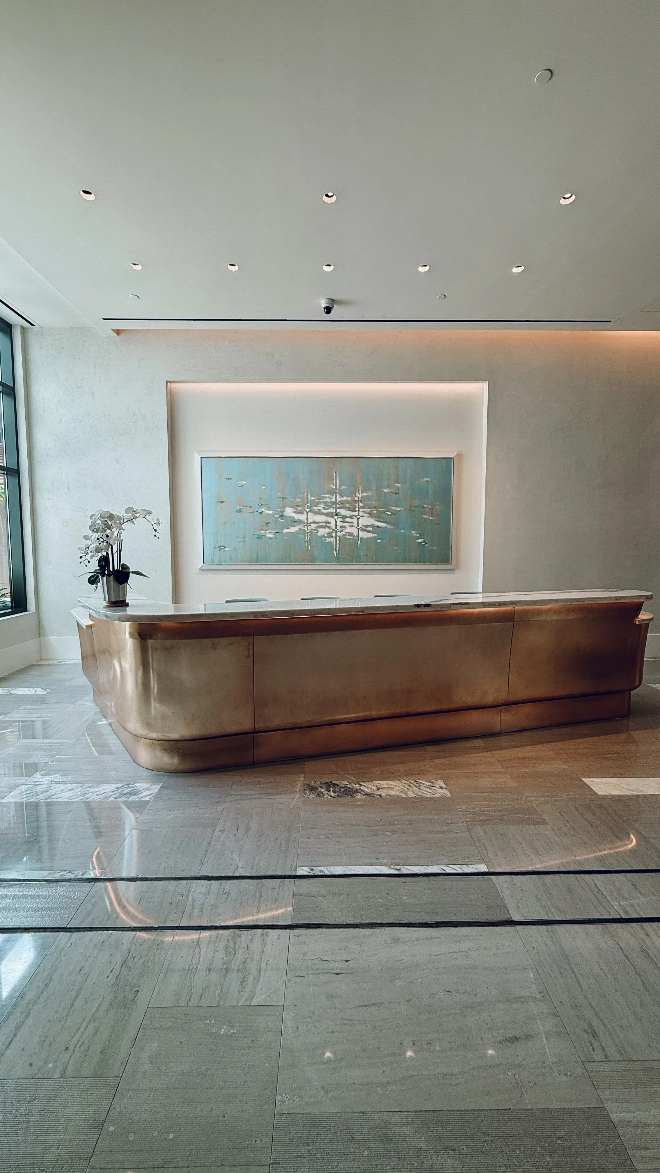 Modern hotel or office lobby reception desk with a large framed artwork, a flower arrangement, and marble flooring.