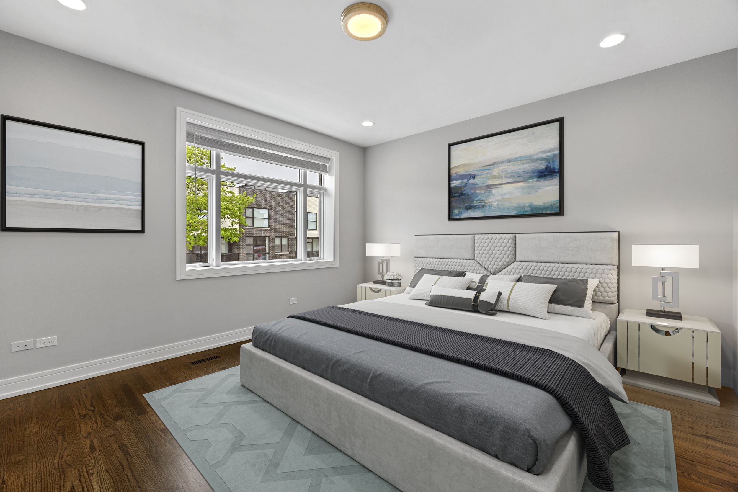 Modern bedroom with a large window, white walls, and minimalist decor. The bed has a tufted headboard, white linens with gray and white pillows, and a dark gray blanket. Two matching nightstands with lamps are on either side of the bed. There are two abstract landscape paintings on the walls, and a light blue geometric rug on hardwood floor.
