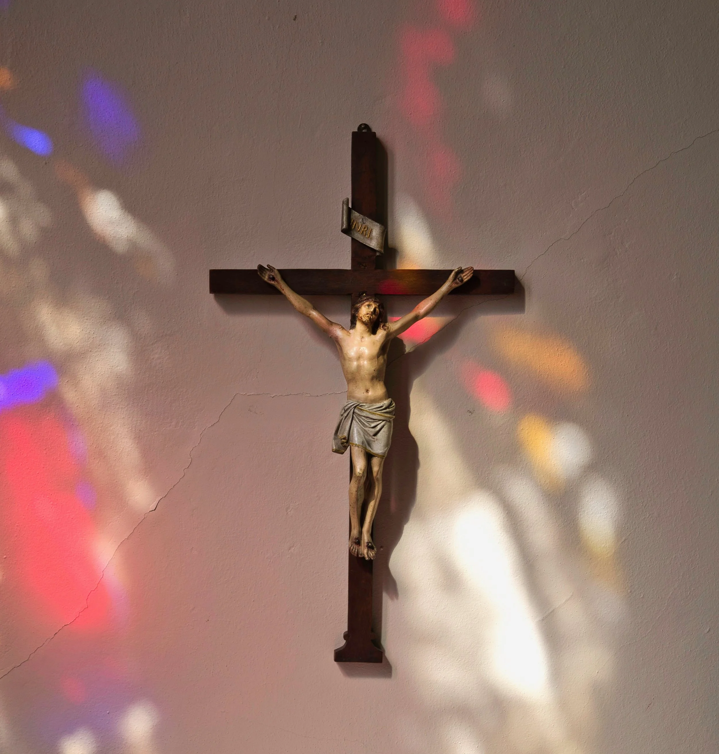 Crucifix featuring Jesus on a cross, mounted on a wall with colorful light reflections.