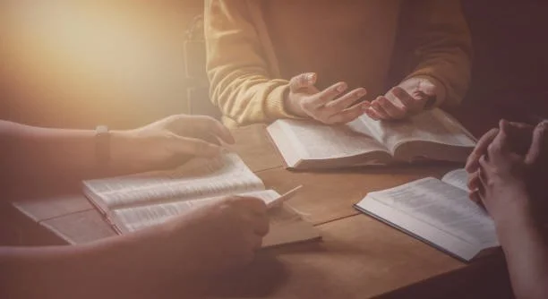 People sitting around a table with open books, engaged in discussion or study.