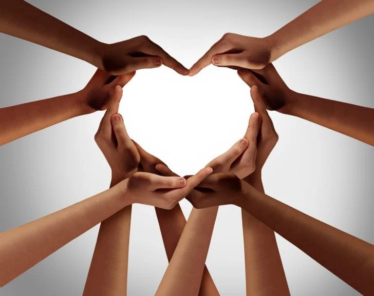 Multiple hands forming a heart shape against a gray background.