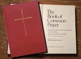 Open Bible with red cover and gold cross, titled 'The Book of Common Prayer' on the page.