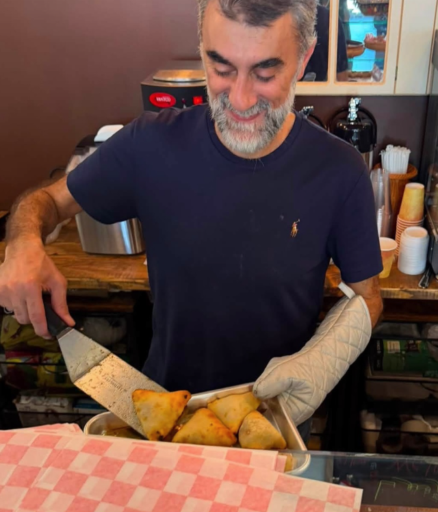 A man in a navy T-shirt is serving freshly fried spring rolls on a tray at a restaurant or cafe.