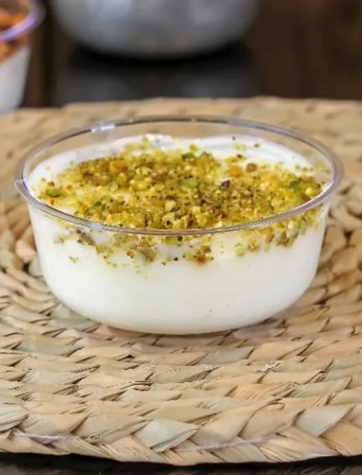 Bowl of creamy dessert topped with chopped pistachios on a woven placemat.
