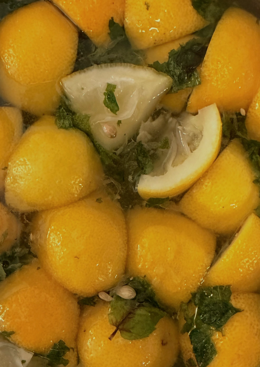 Lemons with mint leaves and seeds submerged in water.
