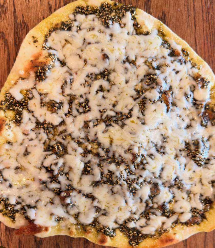 Close-up of a pizza with cheese and black sesame seeds on a wooden surface.
