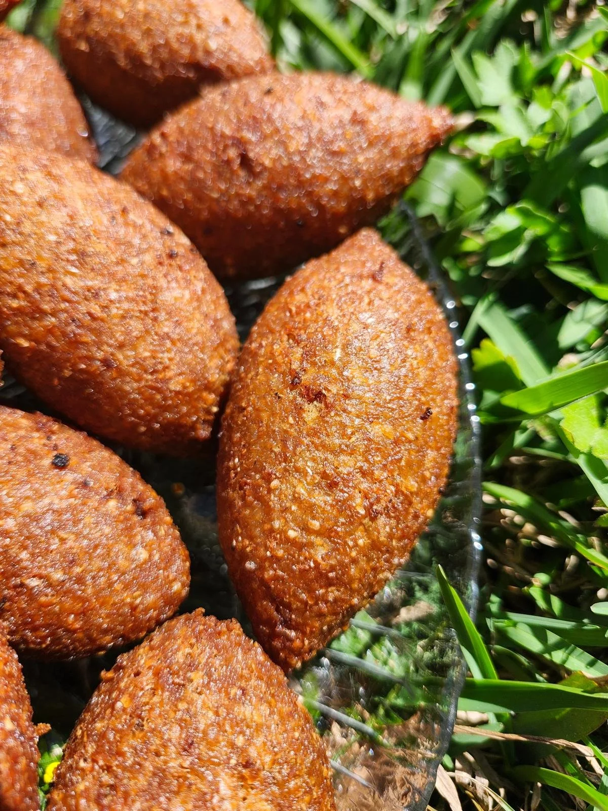 Fried croquettes arranged on a glass tray outdoors among green grass.