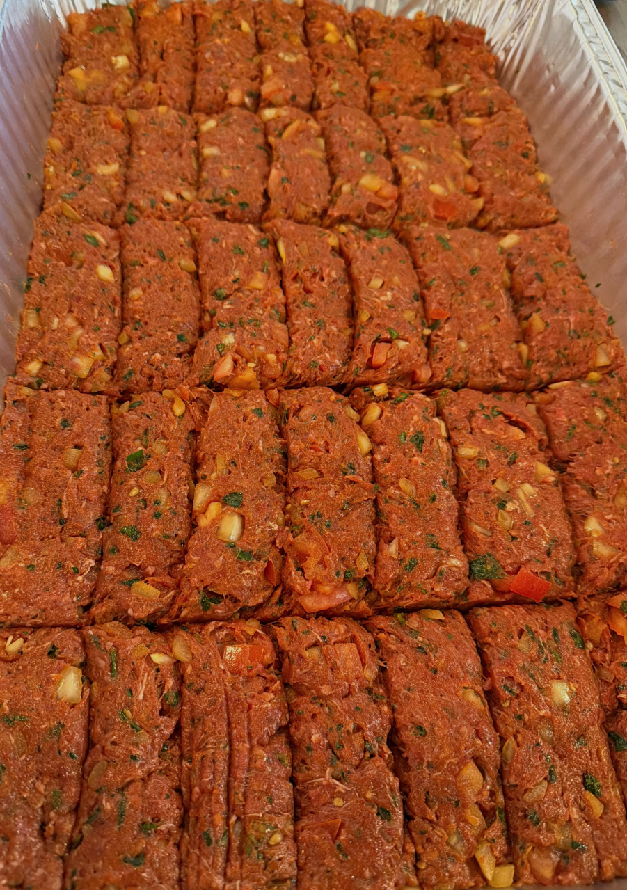 Tray of raw, seasoned meatloaf mixture shaped into rectangular portions, prepared for cooking.