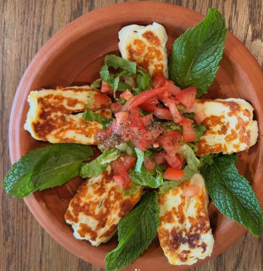 A plate of grilled cheese sandwiches with fresh mint leaves and a salad with chopped tomatoes and herbs on top.