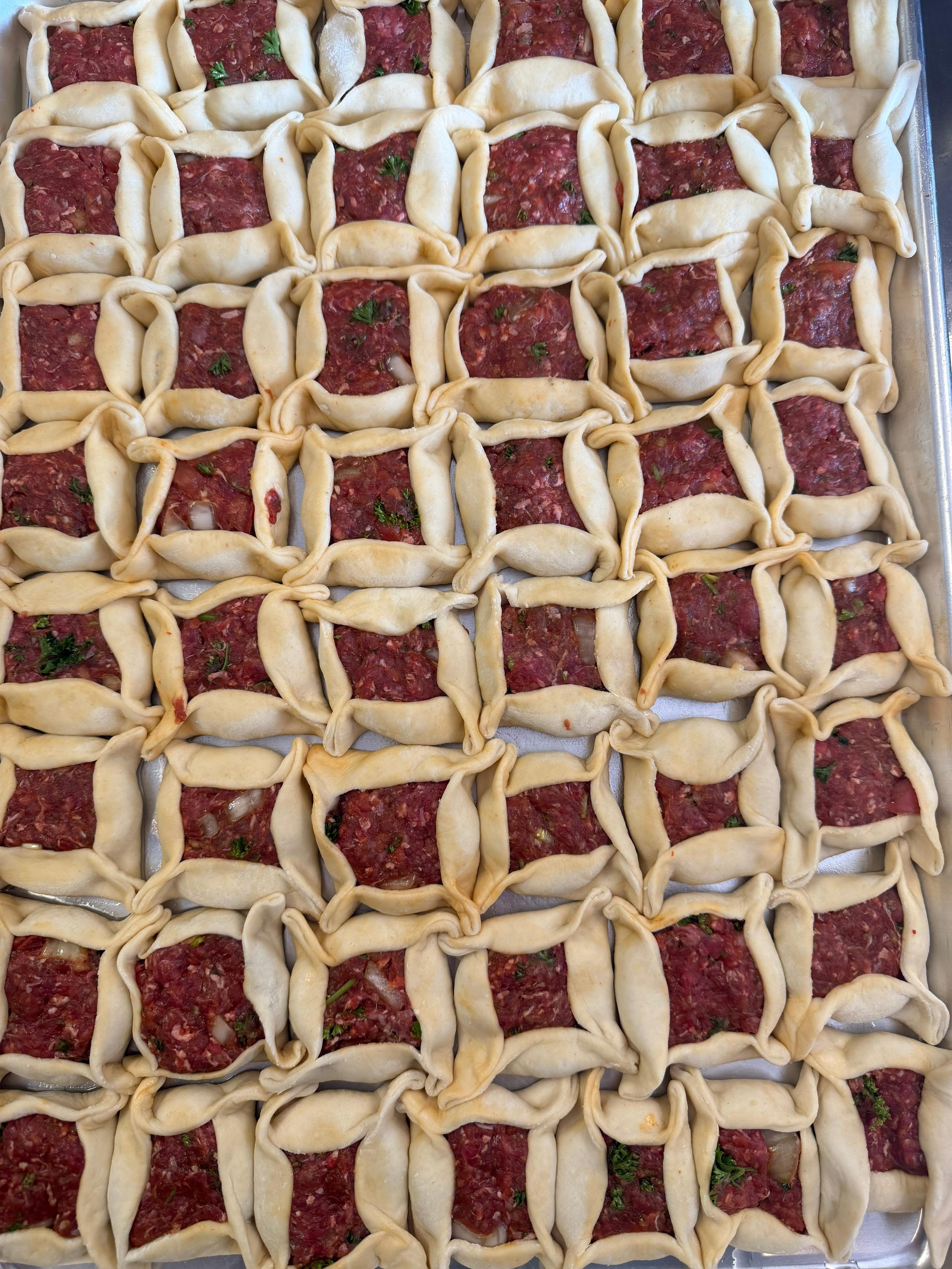 Unbaked beef Wellington pastry with raw chopped beef and herbs in a basket weave pattern.