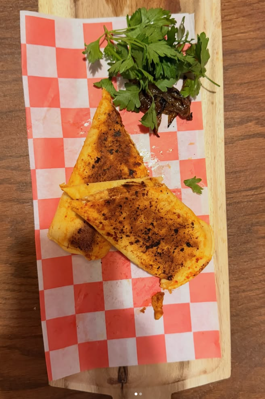 Grilled quesadillas served on a red and white checkered paper on a wooden board, garnished with fresh parsley and caramelized onions.