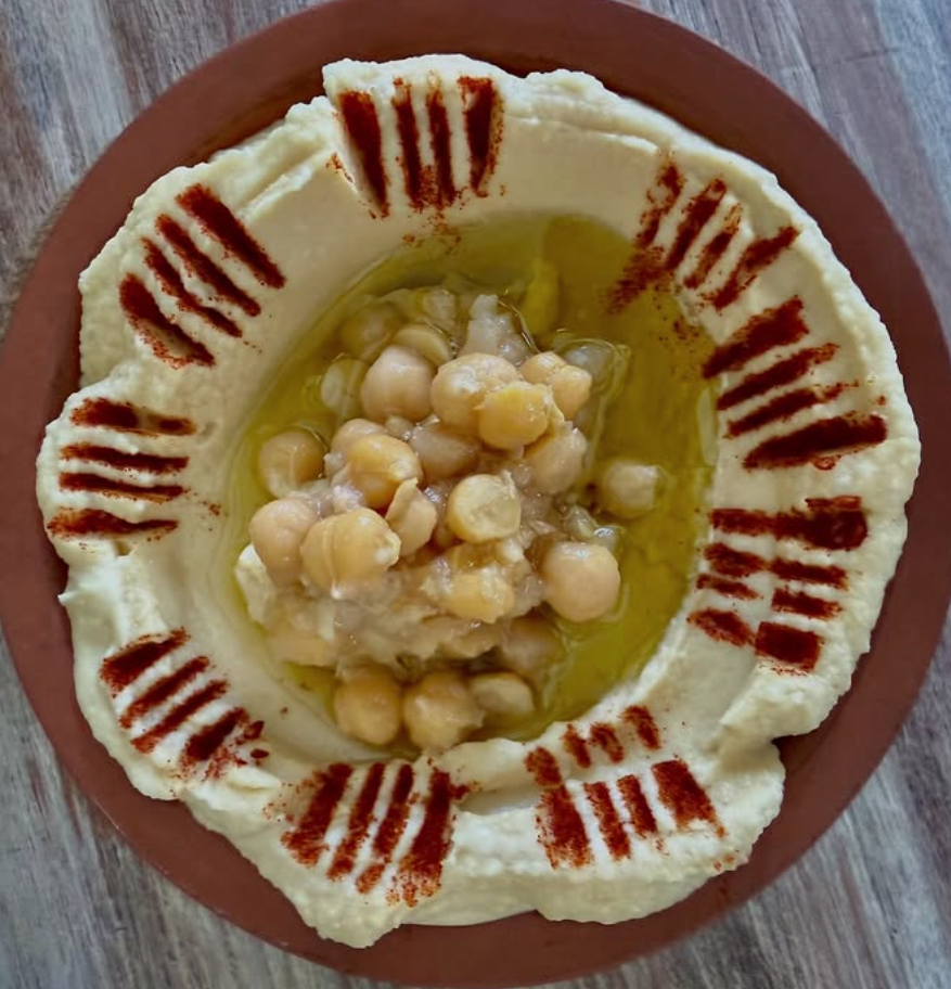 Plate of hummus topped with chickpeas, with a ring of olive oil and paprika garnish around the edge.