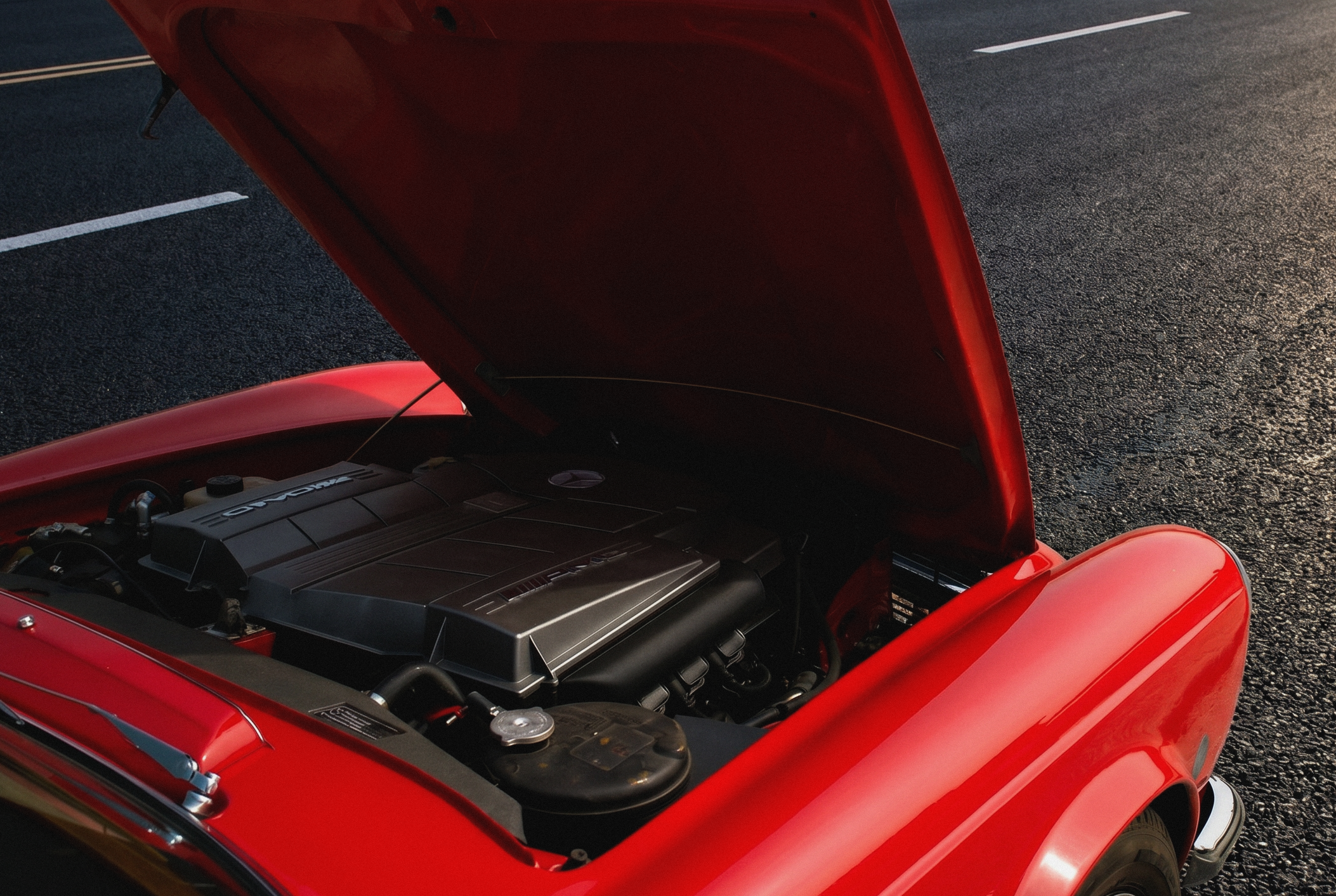 Close-up of a red vintage sports car with its hood open, revealing the engine, parked on an asphalt surface.