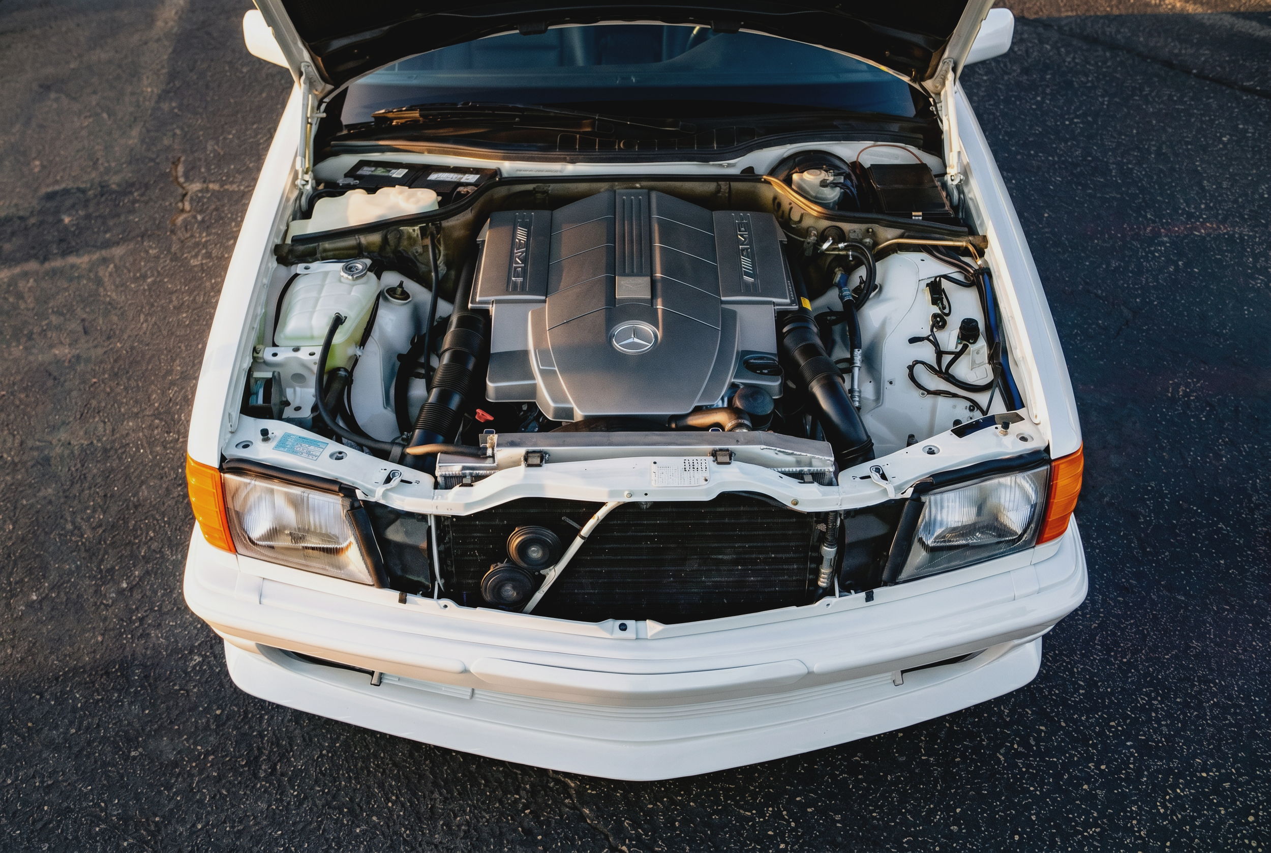 Top view of the open hood of a white Mercedes-Benz car showing the engine and engine bay.