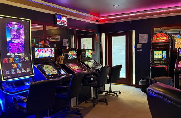 Interior of a small arcade with multiple electronic gaming machines, some showing colorful graphics, illuminated by vibrant neon lighting.
