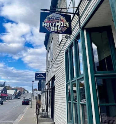 Sign for Holy Moly BBQ hanging outside a building on a street.