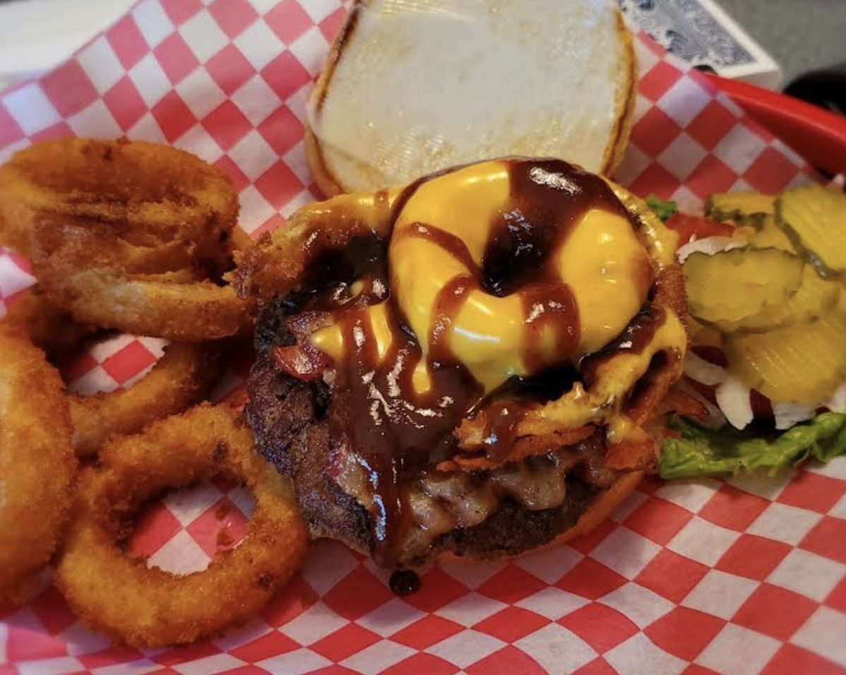 Cheeseburger with onion rings and pickles, served with a sesame seed bun on red and white checkered paper