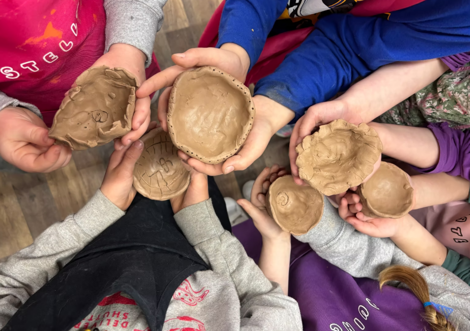 Children holding up handmade clay bowls they crafted.