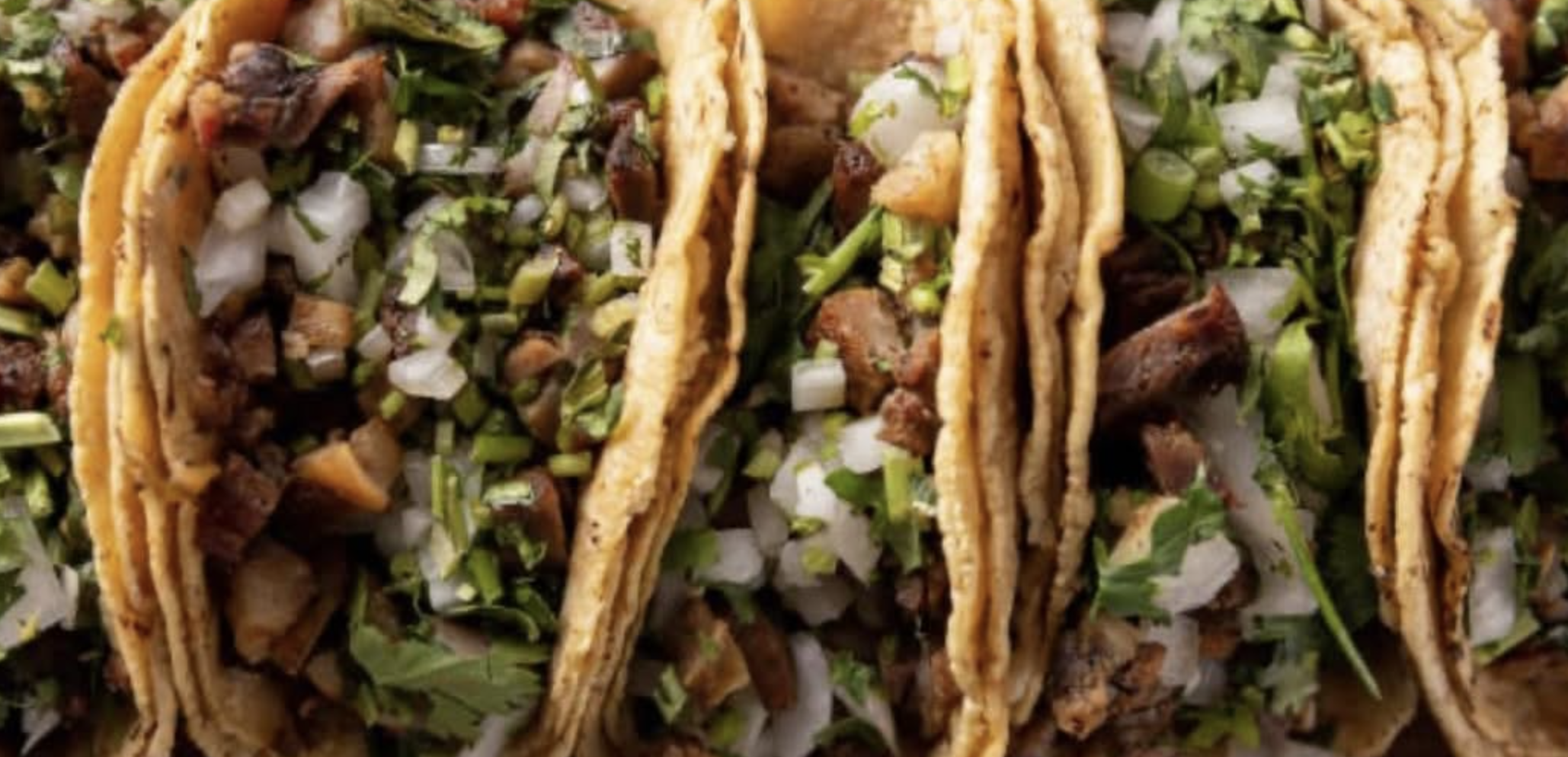 Close-up of three beef tacos filled with chopped meat, onions, and chopped green herbs.
