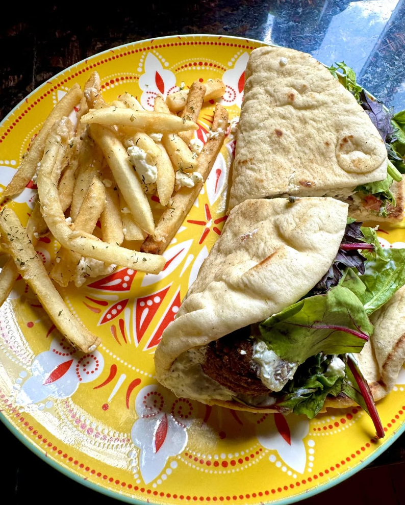 A plate with French fries and a wrap sandwich filled with greens and meat.