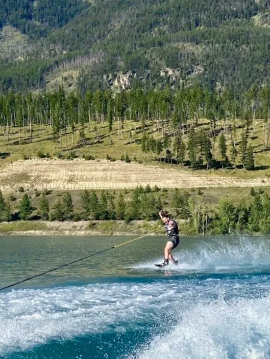 A person waterskiing on a lake with a mountainous forested background.