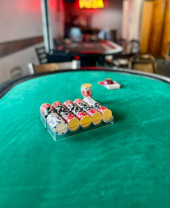 Poker chips arranged on a green poker table with a blurred background of a restaurant or bar setting.