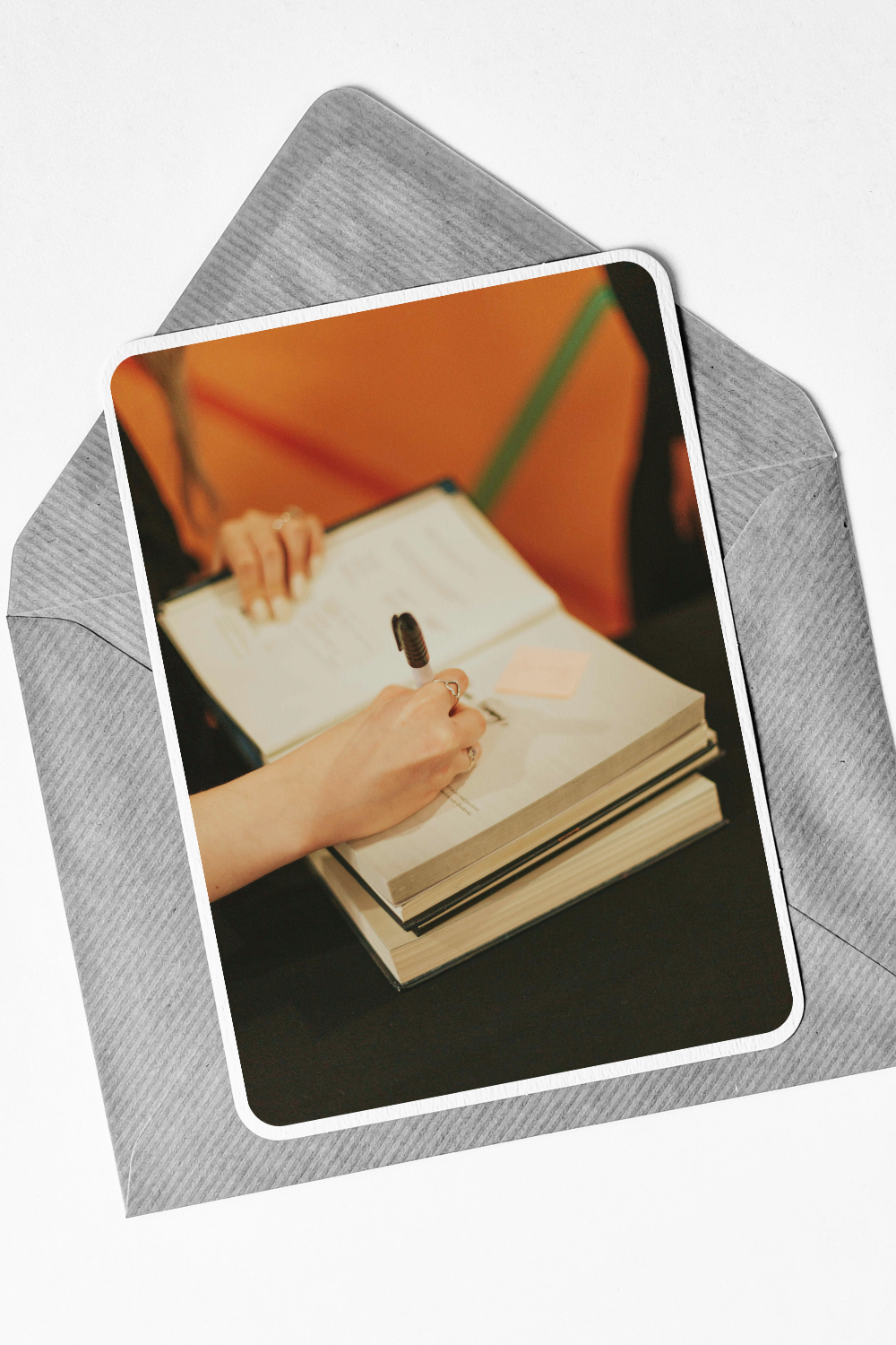 Person writing in a notebook on top of two stacked books, with colorful background.