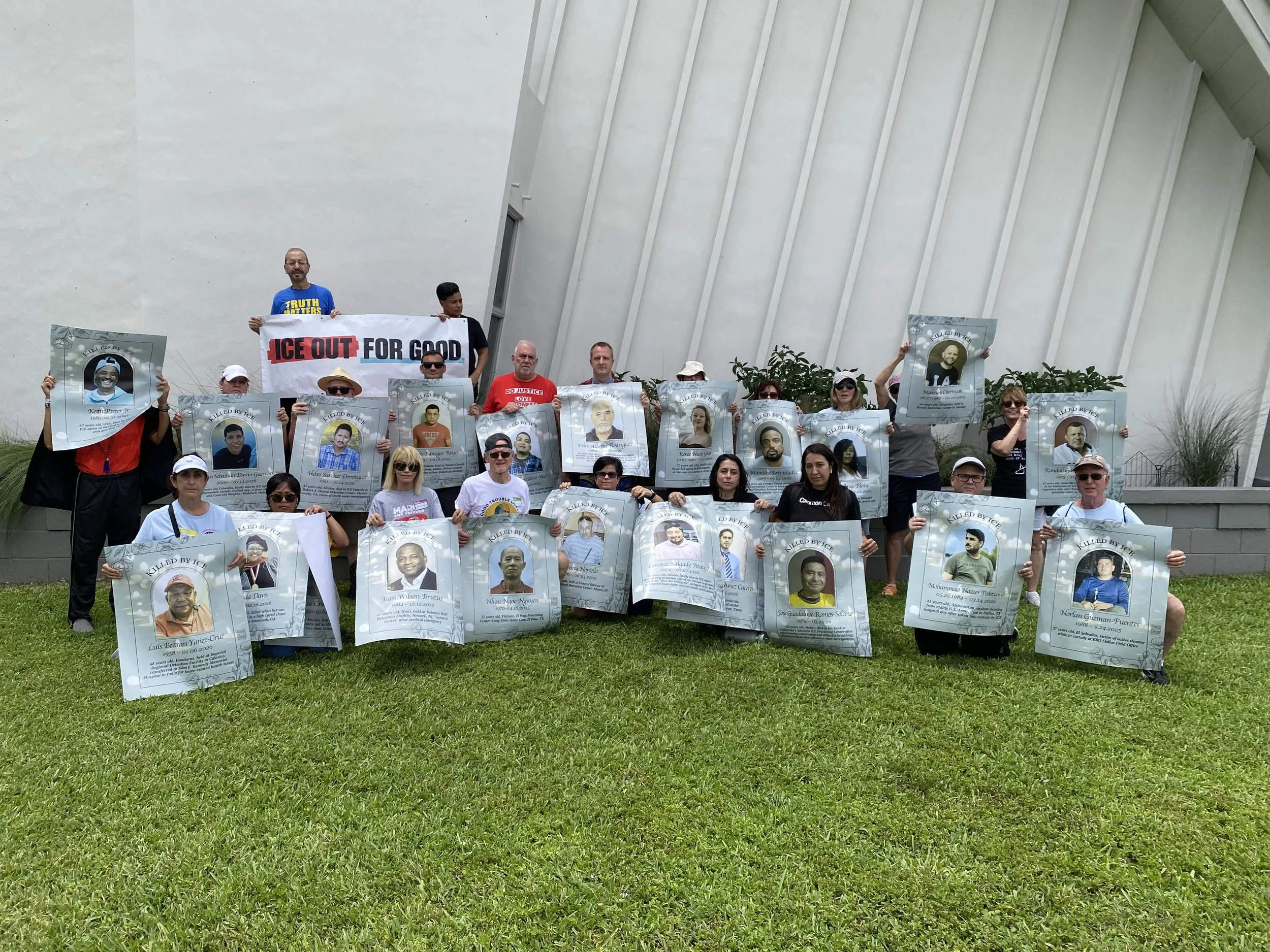 Group of people holding posters with images and names of individuals who appear to have been victims of violence or injustice.