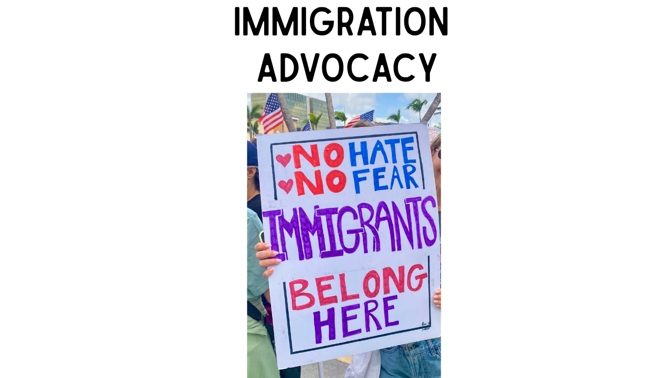 A Protest Sign with American flags and people in the background. No Hate No Fear Immigrants Belong Here