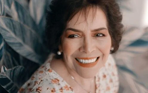 A woman with short curly hair smiling and looking to the side, wearing earrings and a patterned top.