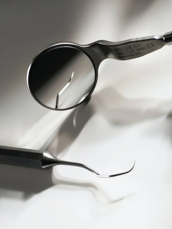 A dental mirror and a dental scaler tool on a white surface.