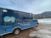 Blue mobile dental hygiene clinic with Mountain Peak to Peak logo and contact information, parked on snowy ground with mountain background