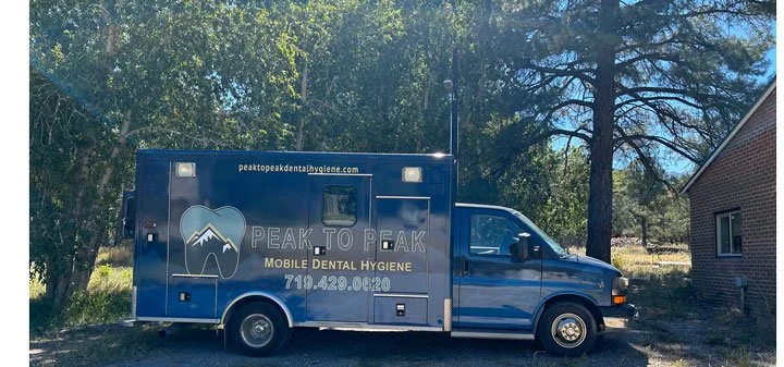 Blue mobile dental hygiene truck parked near a house with trees in the background.