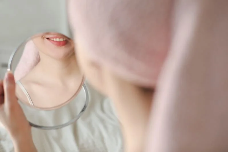 A person holding a mirror, reflecting their smiling face.