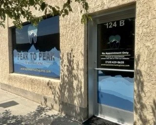 Peak to Peak Dental Hygiene, PC storefront with a window sign and a door sign, both featuring mountain and lake graphic designs, with the words 'Peak to Peak' and contact information for an appointment-only business.