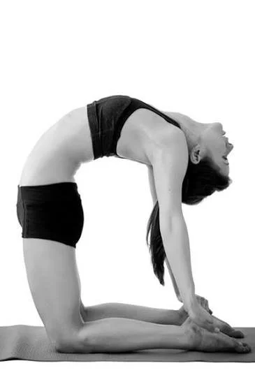 Woman performing a yoga pose on a yoga mat, with her back arched and hands and feet on the mat.
