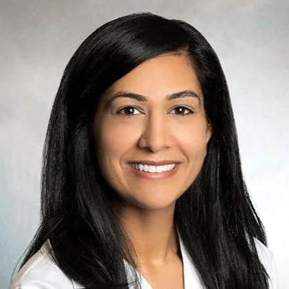 Professional portrait of a woman with long black hair, smiling, wearing a white top.