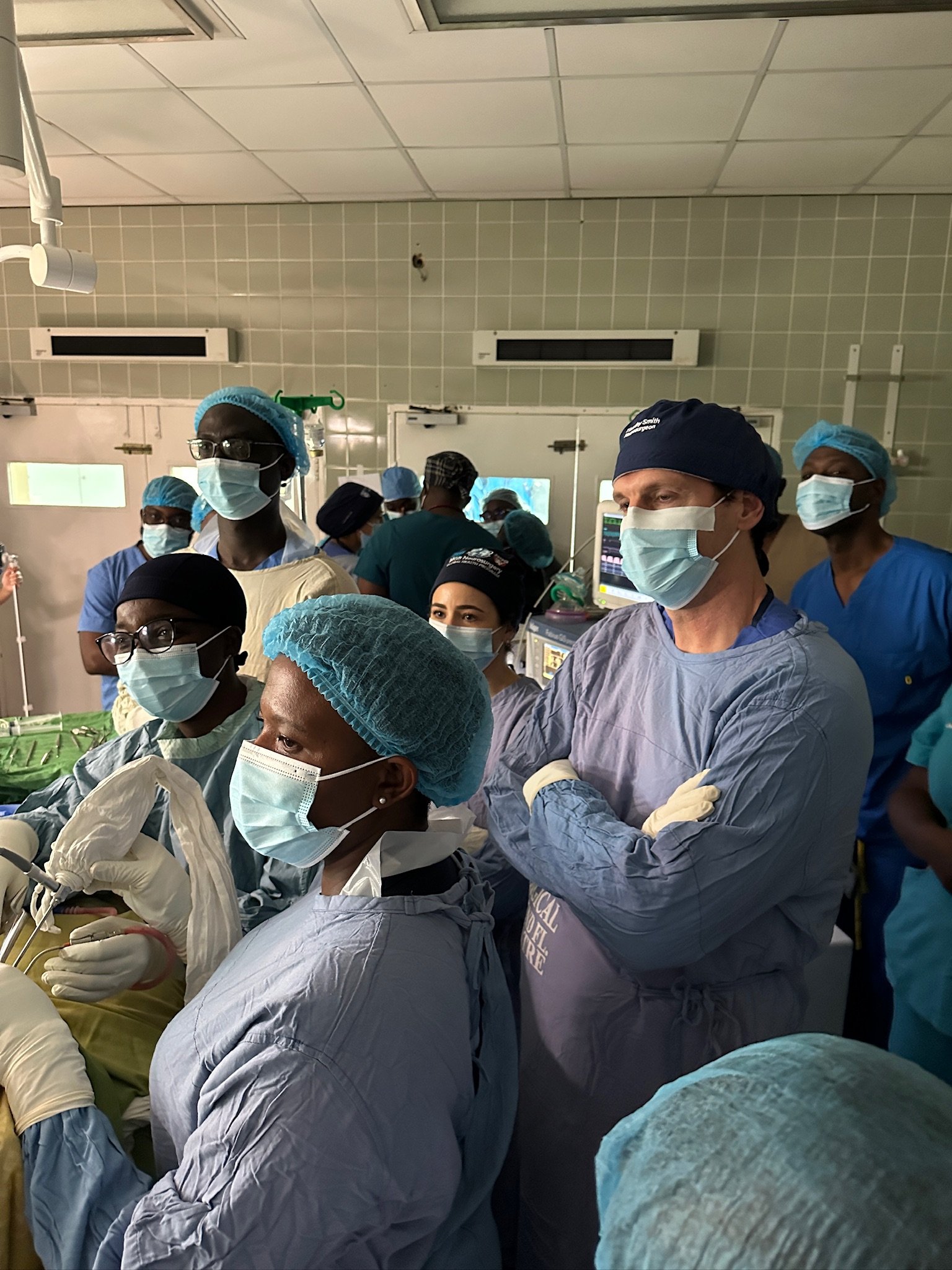 Group of healthcare professionals in surgical scrubs, masks, and caps assembling in an operating room.