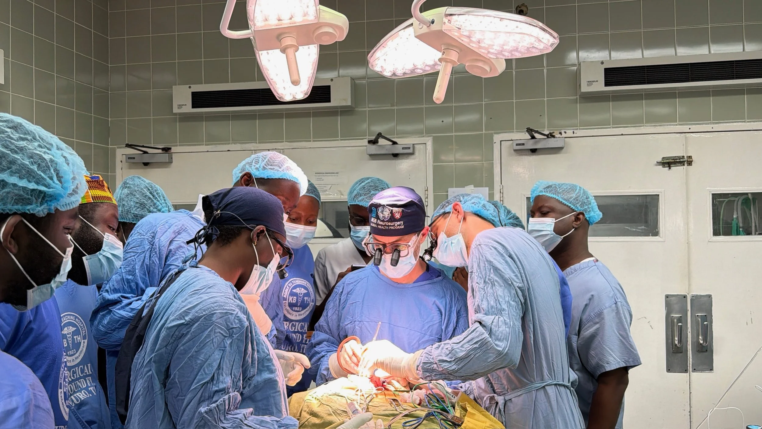 A group of medical professionals dressed in scrubs and surgical masks performing surgery in an operating room, using surgical instruments and focused on the procedure.