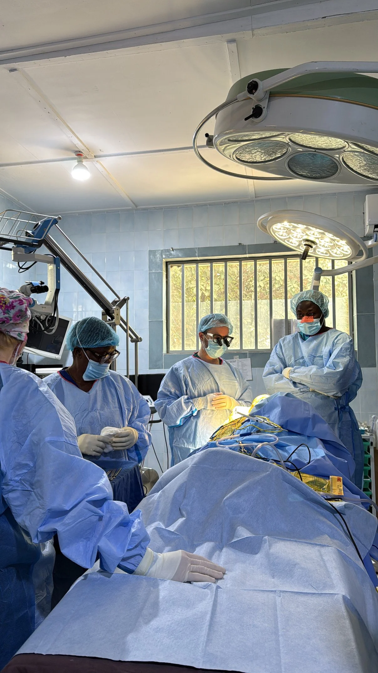 A team of medical professionals, dressed in surgical scrubs, masks, and gloves, performing surgery in an operating room under bright lights, with medical equipment and monitors visible.