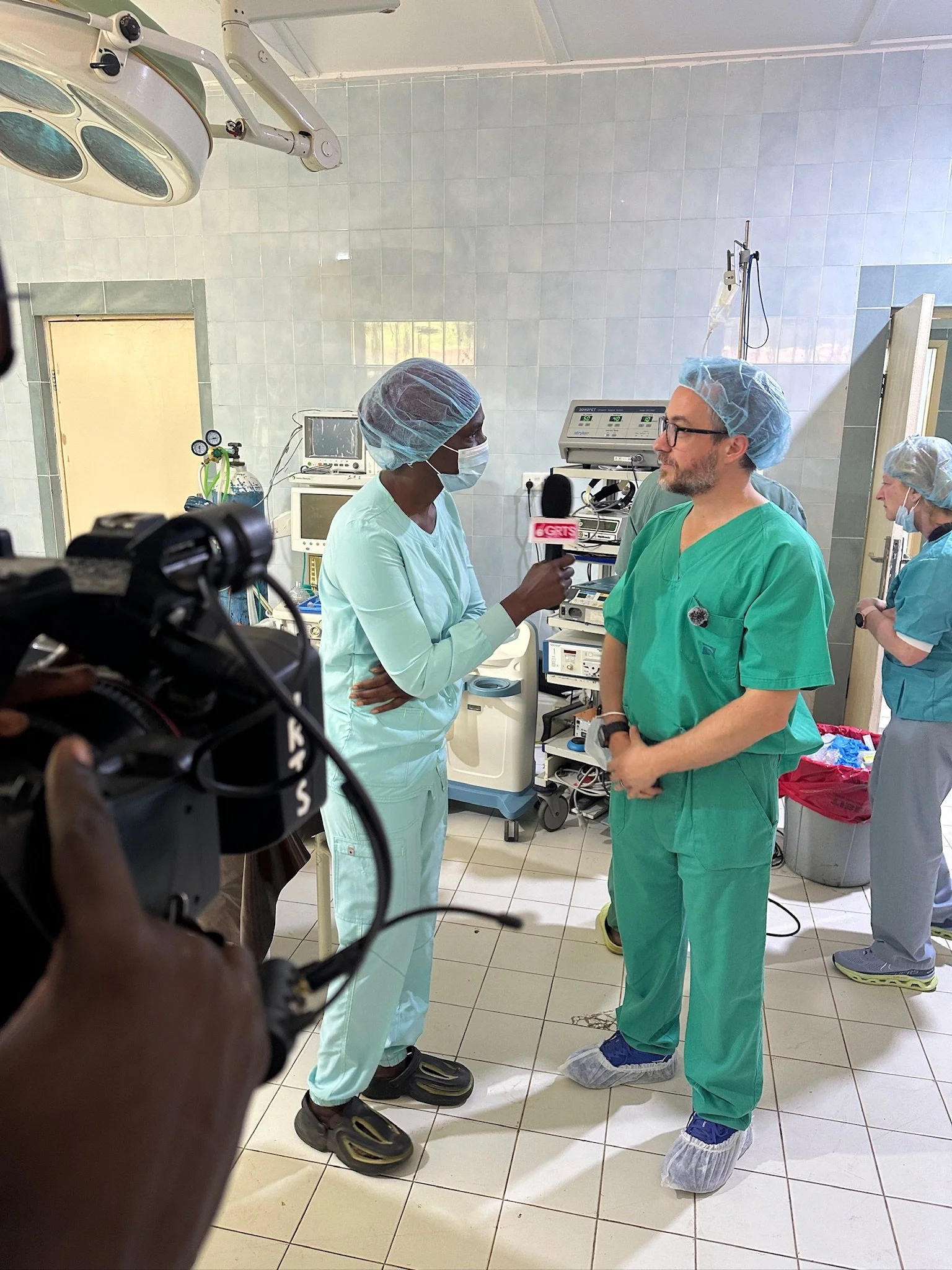 Medical staff and doctor in surgical scrubs and hair covers inside an operating room, preparing for a medical procedure.