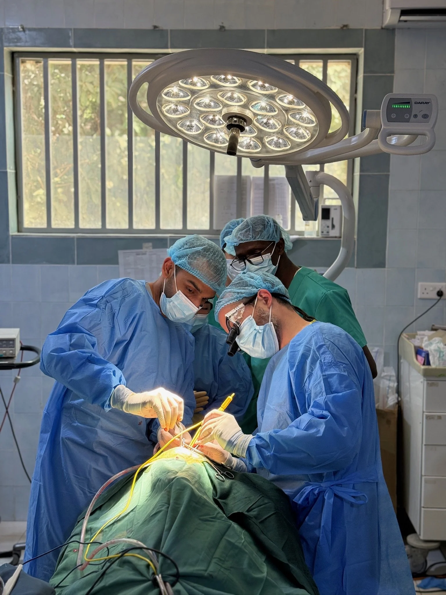 A team of surgeons performing surgery in an operating room with bright light overhead and medical equipment around.