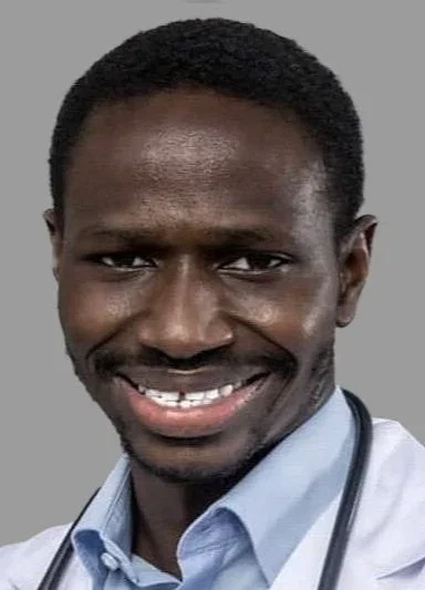 Close-up of a smiling man with dark skin, short black hair, wearing a light blue shirt and a stethoscope around his neck.