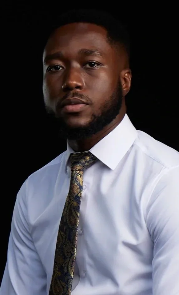 Portrait of a man wearing a white shirt and a patterned tie, against a black background.