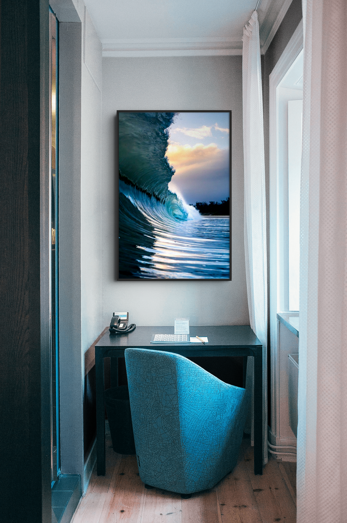 A small office space with a desk, a chair, a telephone, and a framed picture of an ocean wave on the wall.