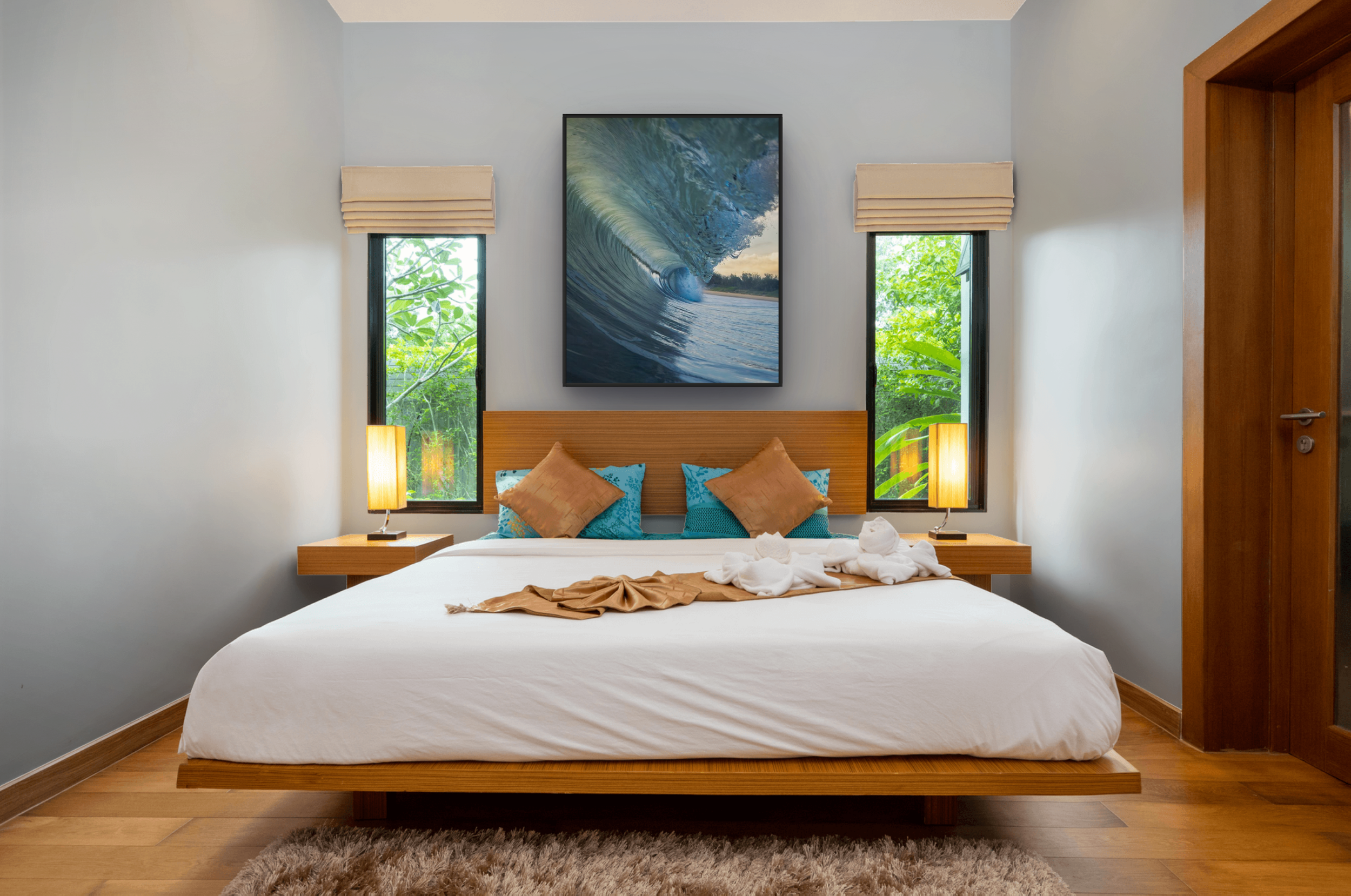 A bedroom with a large bed, two nightstands with lamps, two small windows with blinds, and a large framed picture of a wave on the wall above the bed.