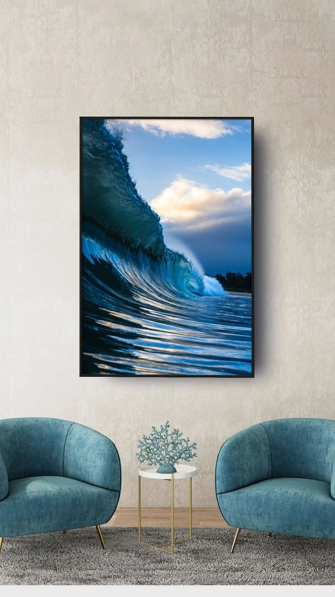 Modern living room with two teal velvet armchairs, a small white and gold side table with a decorative coral sculpture, a rug, and a large framed photograph of a large ocean wave with blue skies on a white wall.