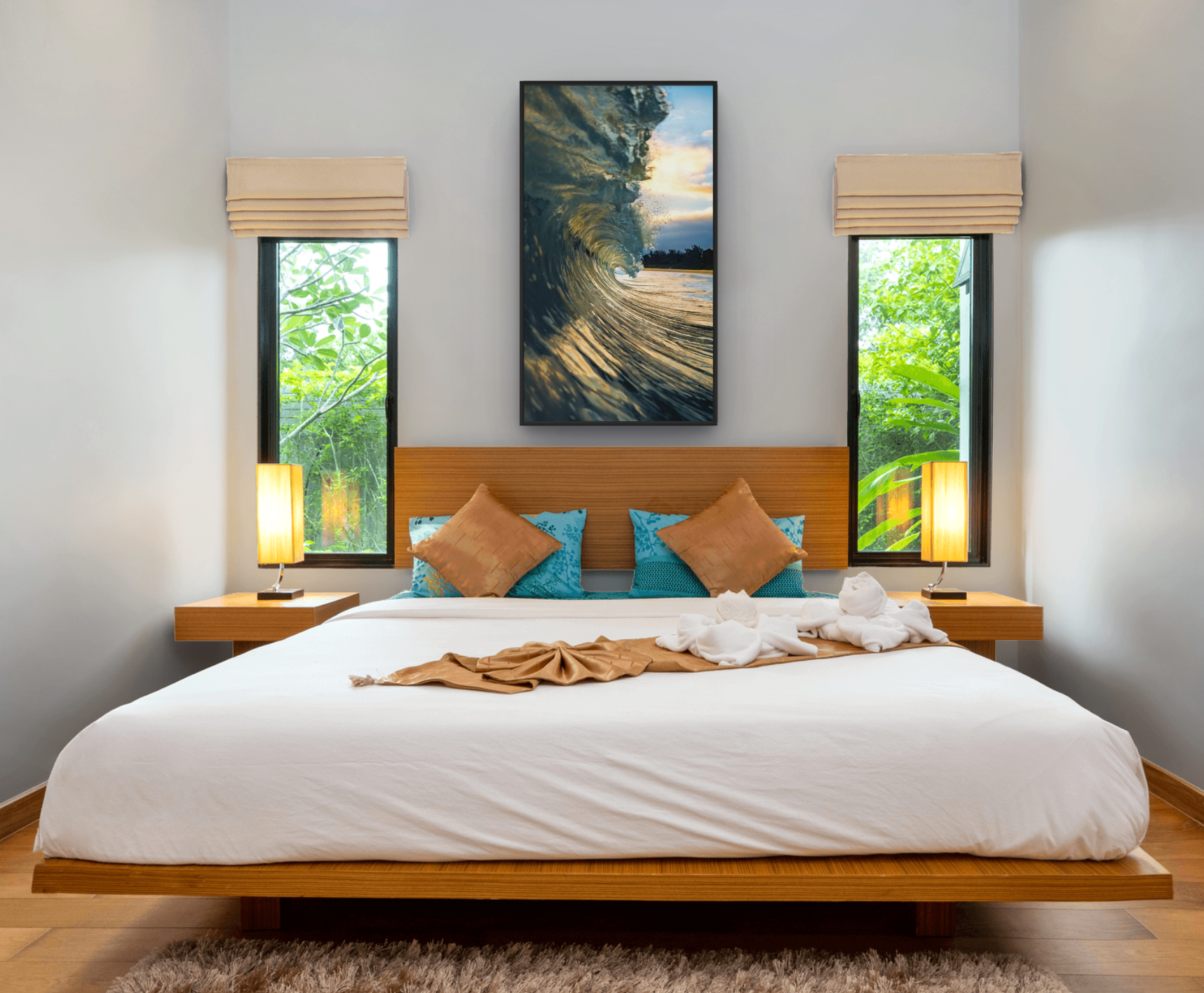 A neatly made bedroom with a large bed, four pillows, and towel art in the shape of a heart. There are two nightstands with lamps on either side of the bed, two windows with beige blinds, and a large ocean-themed painting on the wall.