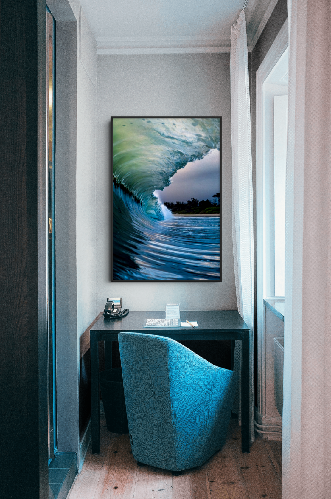 A small office workspace with a desk, chair, and a large framed picture of a wave on the wall.